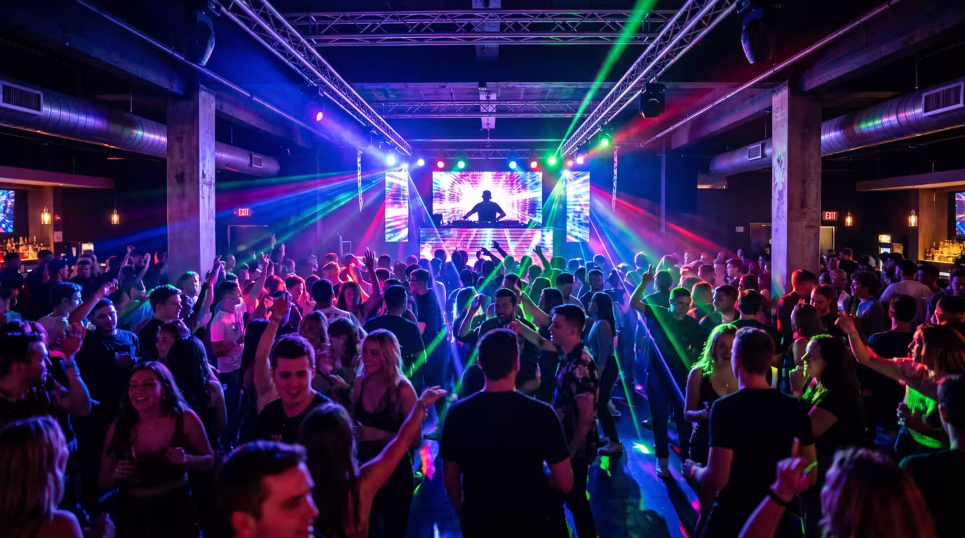 A busy nightclub with a DJ and dancing crowd under stage lighting