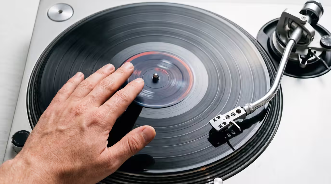 Overhead view of a hand on a vinyl record with the tonearm visible